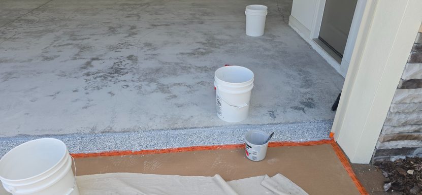 Three paint buckets and a small cup on a concrete surface with a brown tarp.