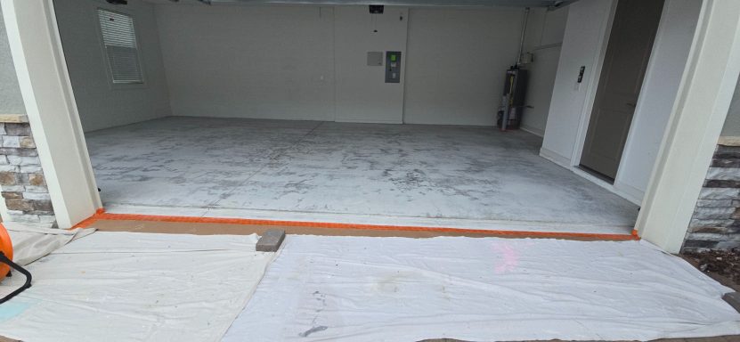 Empty garage space with a white floor and orange marking near the entrance.