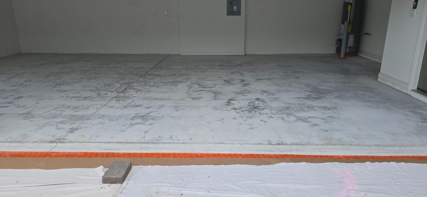 Empty concrete garage floor with a faint pattern, partially covered by a plastic sheet.